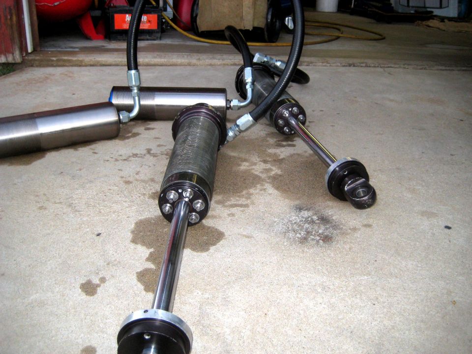 Three hydraulic shock absorbers with hoses on a concrete floor