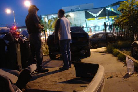 1993 Ford Taurus - Two men converse near the back of a sedan, with another vehicle visible behind it.
