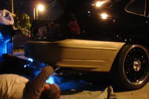 1993 Ford Taurus - A person works on the exhaust system of a car at night, illuminated by blue lights.