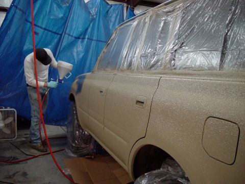 1978 Ford Bronco - A person is spray painting an SUV inside a booth made of blue tarps and plastic sheeting.