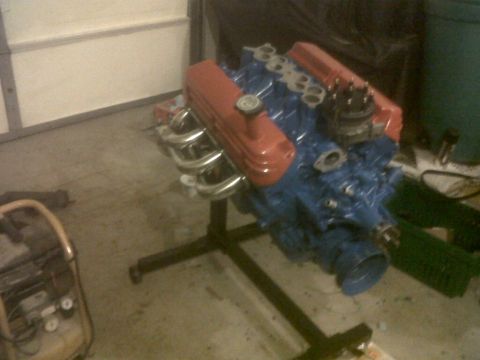 1989 Ford Mustang - A V8 engine, painted blue with orange valve covers, sits on a stand in a garage setting.
