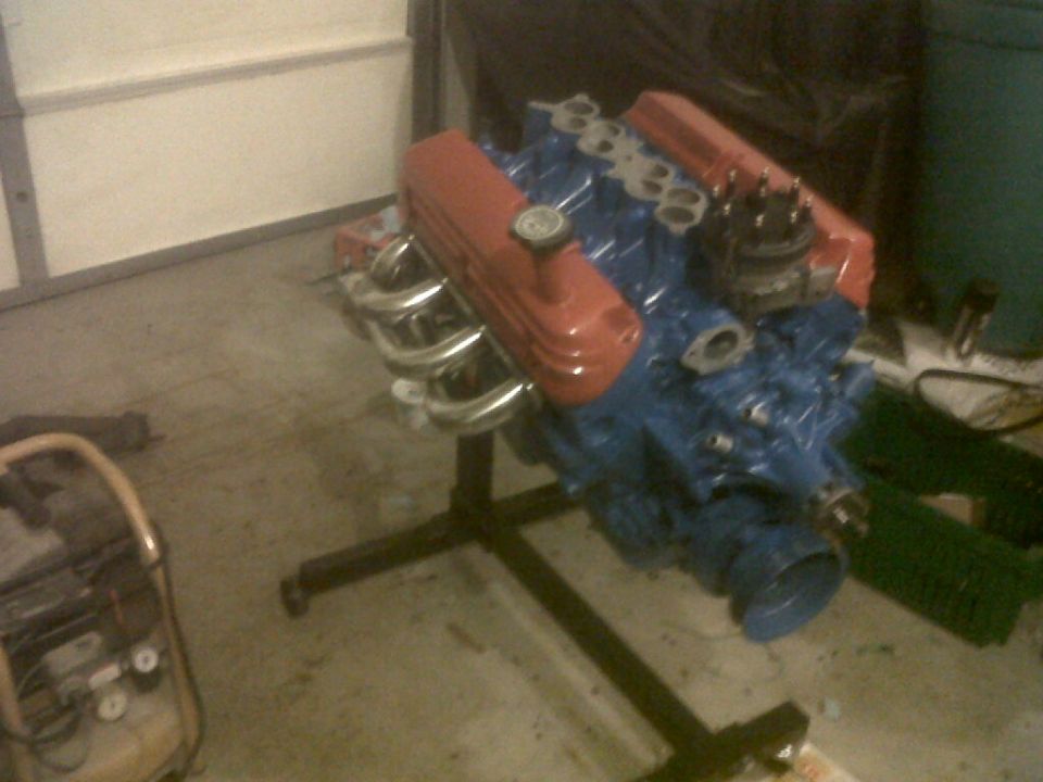Blue V8 engine with orange valve covers on a black stand in a garage