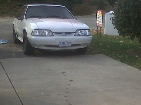 1989 Ford Mustang - This white 1989 Ford Mustang is parked in a driveway, with a 'For Sale' sign visible in the background.
