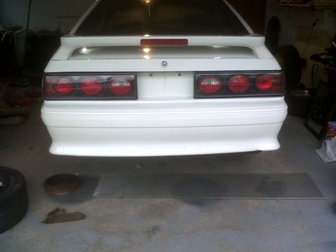 1989 Ford Mustang - The rear end of a white coupe is shown, possibly undergoing maintenance or restoration.