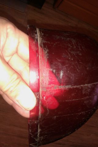 1991 Ford Crown Victoria - A hand holds a red taillight assembly, revealing its internal components and the scratched condition of the lens.