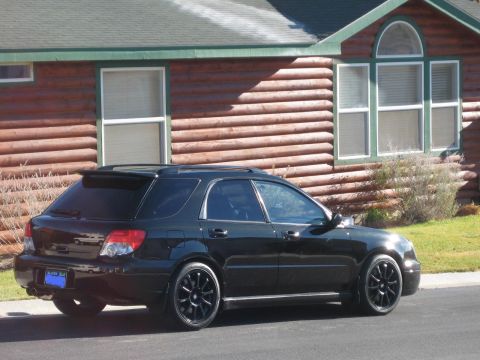 2005 Subaru Impreza - A black Subaru Impreza wagon is parked outside a log cabin with a dark green roof.