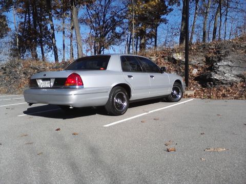 2000 Ford Crown Victoria - A silver 2000 Ford Crown Victoria is parked in a lot with trees in the background.