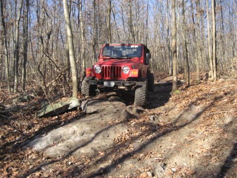 1991 Ford Bronco - Red Jeep Wrangler TJ climbs over rocks on a wooded trail.