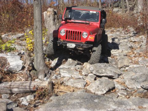 1991 Ford Bronco - Red Jeep Wrangler tackling a challenging rocky off-road path.