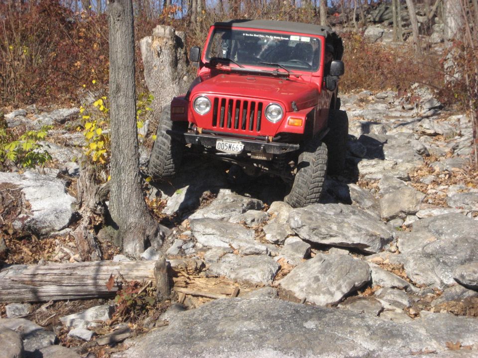 Red Jeep Wrangler navigating a rocky trail, front grille visible