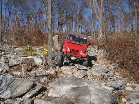 1991 Ford Bronco - A red Jeep Wrangler tackles a challenging rocky terrain during an off-road excursion.