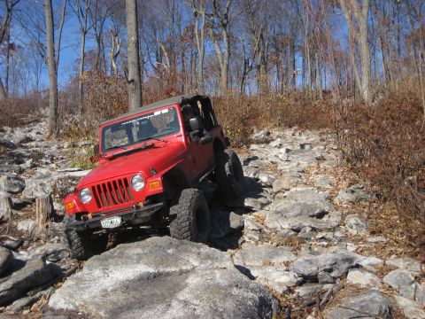 1991 Ford Bronco - A red Jeep Wrangler navigates a challenging rocky terrain on an off-road trail.