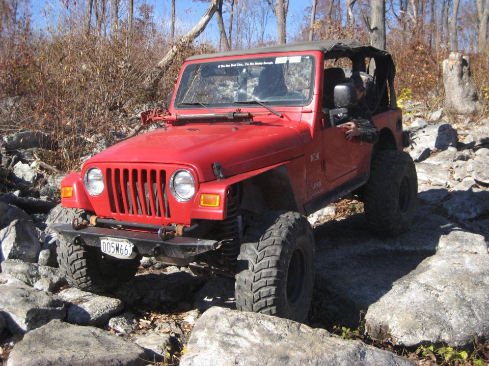 Red Jeep Wrangler TJ with aftermarket bumper and large tires navigating rocks