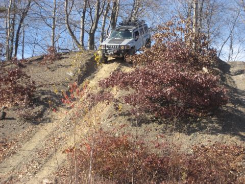 1991 Ford Bronco - A silver Hummer H3 navigates a steep, wooded incline during an off-road excursion.