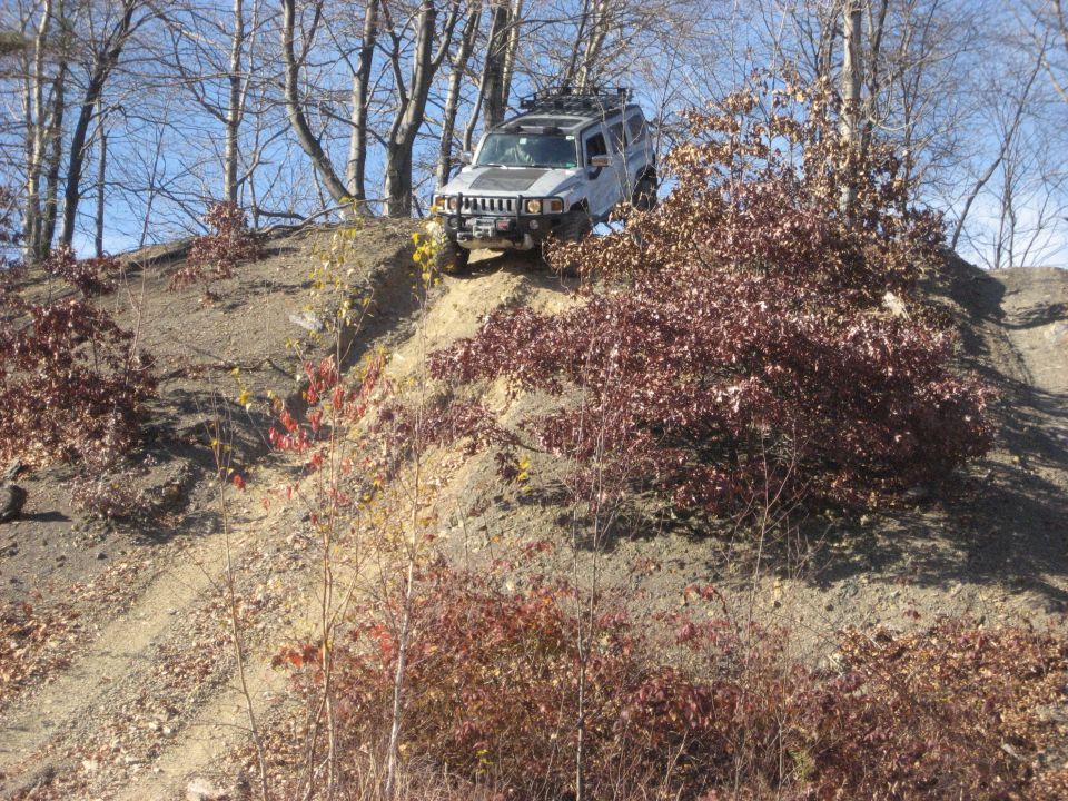 Silver Hummer H3 cresting a steep dirt hill at an off-road park