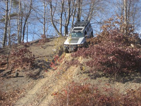 1991 Ford Bronco - Silver Hummer H3 navigates a challenging off-road trail during daylight hours.