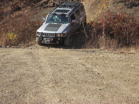 1991 Ford Bronco - A silver Hummer H3 navigates an off-road trail with dense foliage on the right.