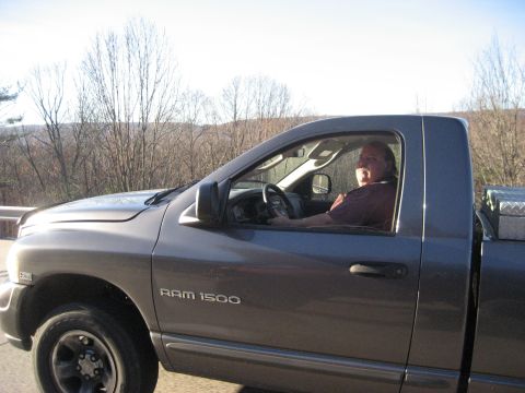 1991 Ford Bronco - Driver in a gray Dodge Ram 1500 pickup truck on a road with trees in the background.