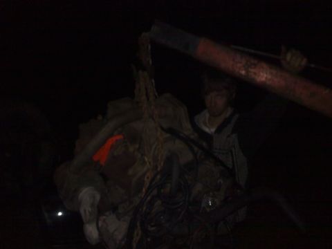 1990 Ford Bronco - A person watches as an engine is hoisted by a crane in a dimly lit environment.