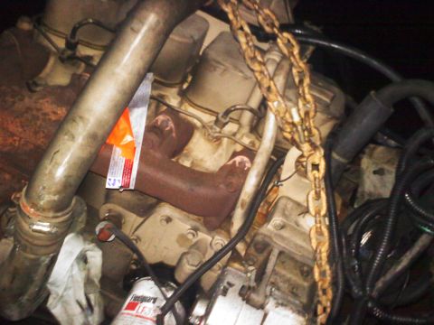 1990 Ford Bronco - Close-up of an engine block, showing exhaust manifold, oil filter, and chains. An orange tag is visible.