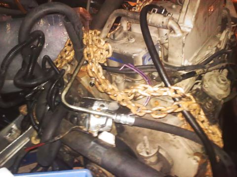 1990 Ford Bronco - Close-up view of an engine compartment with various hoses and a prominent chain.