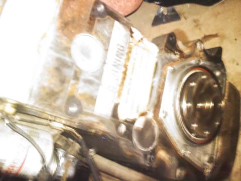 1990 Ford Bronco - A close-up of an engine component a prominent warning sticker and a bolted circular plate.