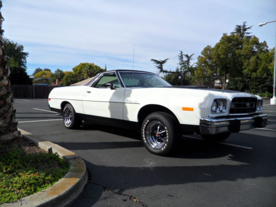 White Ford Ranchero parked in a lot, black hood accent, chrome wheels, Goodyear tires