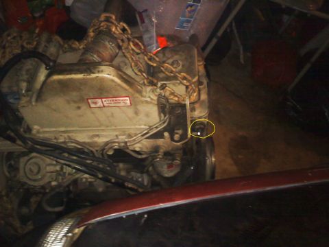 1990 Ford Bronco - Close-up of an engine with a chain wrapped around it, partially obscured by a red car hood.