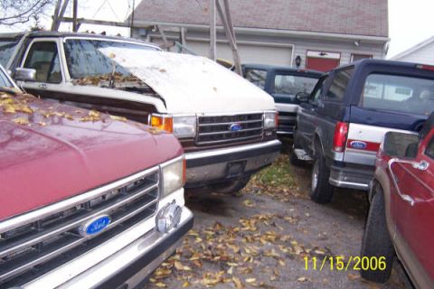 1996 Ford Bronco - Several vehicles are parked in a lot with fallen leaves scattered around.