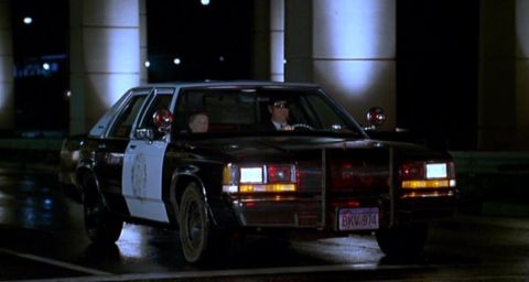 1991 Ford Crown Victoria - A police car is parked at night, illuminated by streetlights and its own headlights.