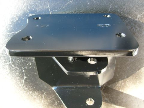 1986 Ford Bronco - A shiny black metal bracket with multiple bolt holes is shown against a textured background.