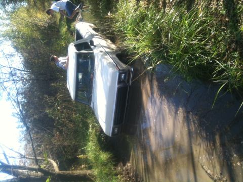 1978 Ford Bronco - A white 1978 Ford Bronco is stuck in a muddy ditch, with two individuals observing the situation.
