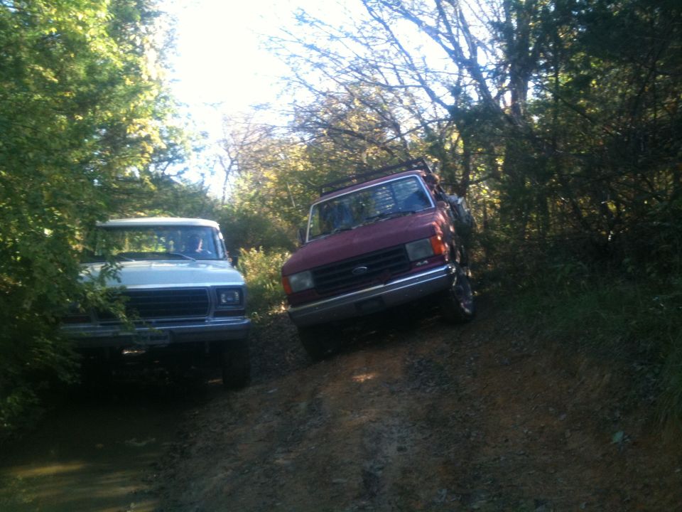 Red truck on a dirt path, front view. White truck behind it