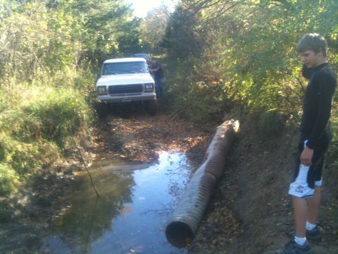 1978 Ford Bronco - 1978 Ford Bronco navigates a muddy off-road trail with a large culvert pipe.