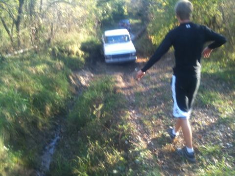 1978 Ford Bronco - A white van navigates a muddy off-road trail, with another vehicle following closely behind.