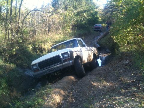 1978 Ford Bronco - A white pickup truck navigates a muddy trail, with another vehicle visible in the distance.