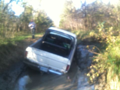 1978 Ford Bronco - A white pickup truck is stuck in a muddy path surrounded by trees.