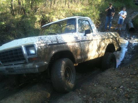 1978 Ford Bronco - A white 1978 Ford Bronco is stuck in a muddy trail with two people standing nearby.