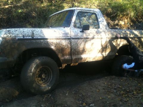 1978 Ford Bronco - A white 1978 Ford Bronco is stuck in the mud, with a person attempting to push it.