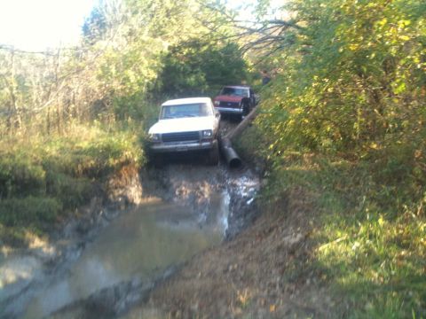 1978 Ford Bronco - Two trucks tackle a challenging muddy path, one appearing to be a 1978 Ford Bronco.