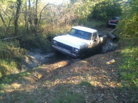 1978 Ford Bronco - A white Ford pickup truck is stuck in a muddy trail, with another vehicle visible in the background.