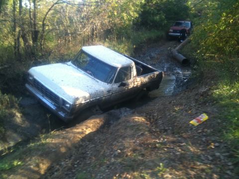 1978 Ford Bronco - A white pickup truck is stuck in a muddy track, with another vehicle visible in the background.