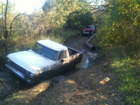 1978 Ford Bronco - A white 1979 Ford F-150 is stuck in a muddy ditch, with a red truck visible in the background.