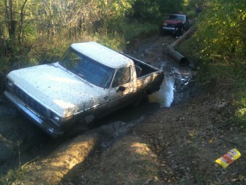 1978 Ford Bronco - A white pickup truck is stuck in a muddy path, with a red truck following behind.
