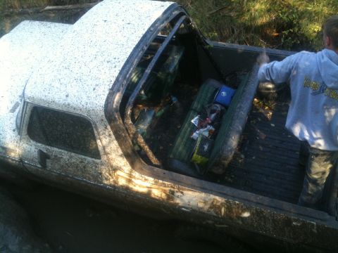 1978 Ford Bronco - A white pickup truck is stuck in mud, with its interior exposed and filled with debris.