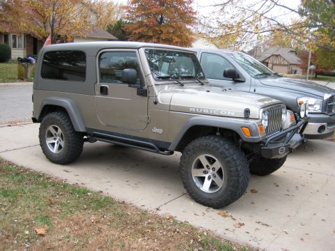 2005 Jeep Wrangler - A tan Jeep Wrangler Rubicon is parked on a driveway next to a grey pickup truck.