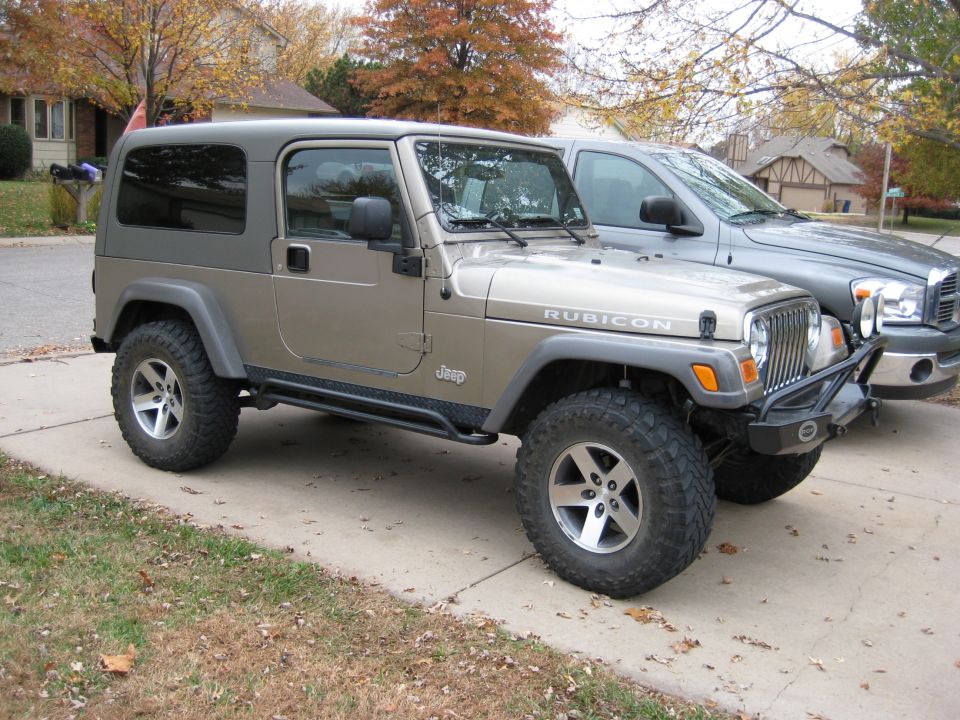 Khaki Jeep Wrangler Unlimited Rubicon with hardtop, rock rails and mud tires on driveway