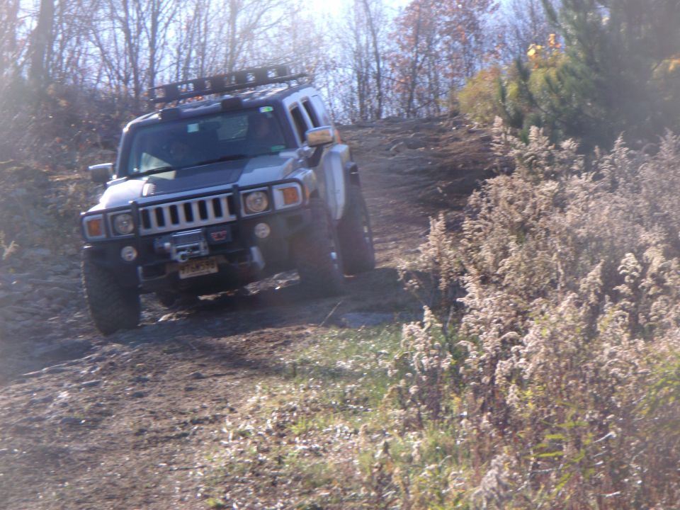 Hummer H3 driving up a dirt hill, front grille and winch visible, roof rack installed