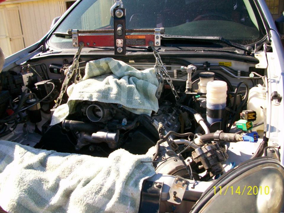 Engine being lifted out of a vehicle with chains and an engine hoist, covered in towels