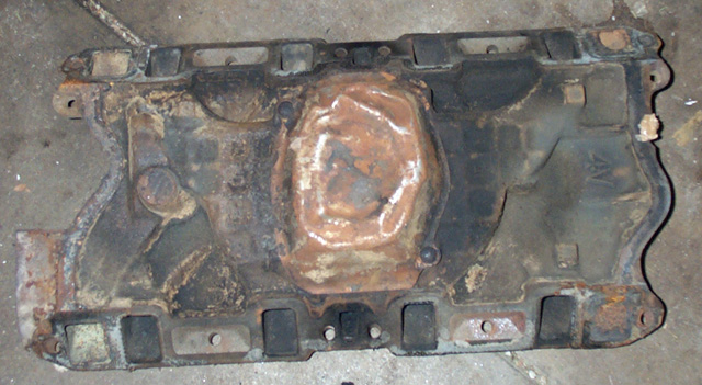 Rusty stamped-steel V8 intake manifold lying upside down on concrete